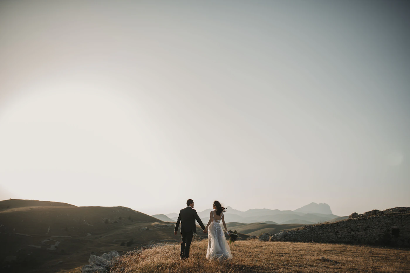 A wedding couple walking hand in hand through an open landscape