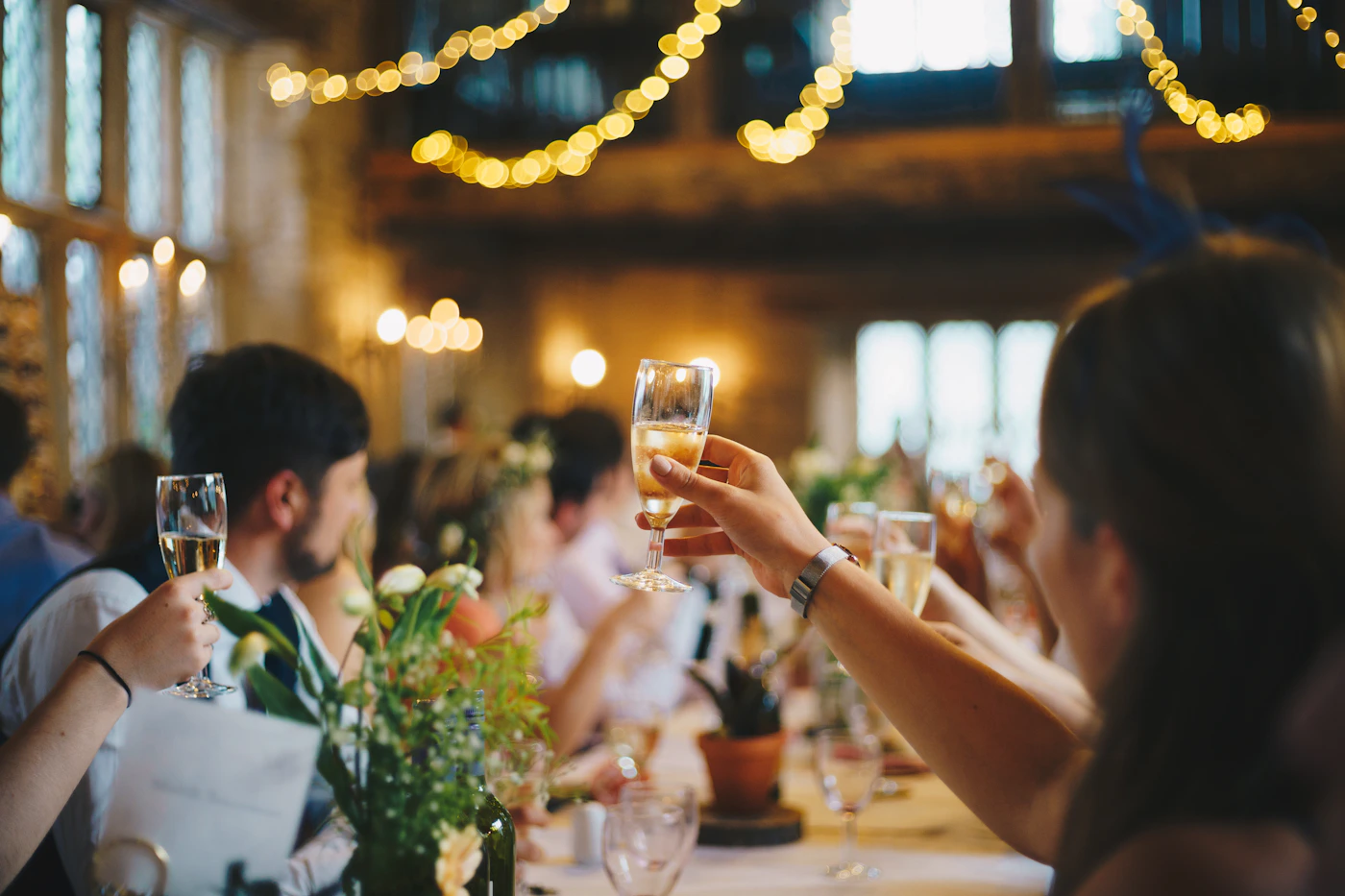 Friends raising their glasses together under warm string lights